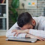 “만성피로, 일상 속 소소한 변화로 극복하기” a man sitting at a desk with his head in his hands