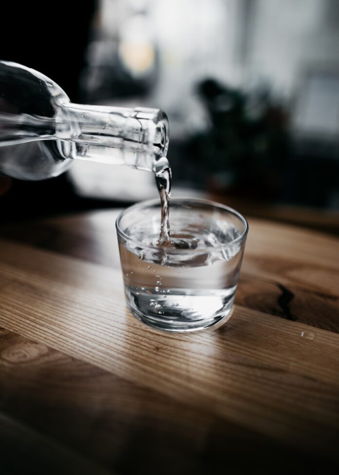 Photo by Brendan Church person holding bottle pouring water on drinking glass